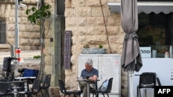 2024年4月14日，一名男子在耶路撒冷的一家路边咖啡馆一边喝早餐的饮料一边看书。
