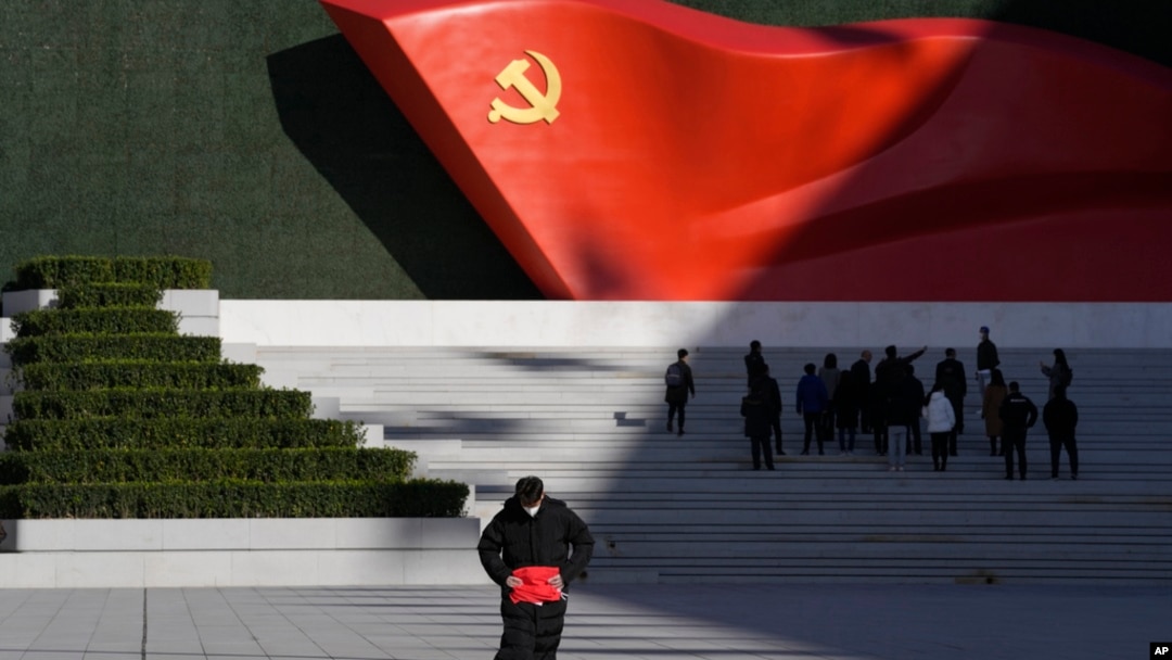 FILE - A worker folds a flag near a giant sculpture of the Chinese Communist Party flag outside the Museum of the Communist Party of China, in Beijing, Nov. 12, 2021.