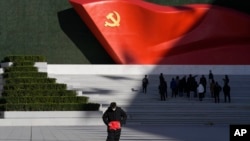 FILE - A worker folds a flag near a giant sculpture of the Chinese Communist Party flag outside the Museum of the Communist Party of China, in Beijing, Nov. 12, 2021.