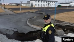 A police officer stands by the crack in a road in the fishing town of Grindavik, Iceland, on Nov. 15, 2023. The town was evacuated because of the threat of a volcanic eruption.