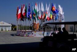 Seorang anggota delegasi diangkut dengan kendaraan kecil melewati deretan bendera negara-negara peserta menuju tempat pertemuan para Menteri Keuangan dan Gubernur Bank Sentral G20 di pinggiran Bengaluru, India, 23 Februari 2023. (AP Photo/Aijaz Rahi)