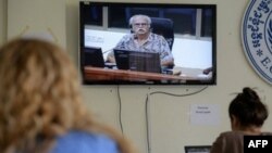 Journalists look at war photographer Al Rockoff (on TV screen) giving evidence to the Extraordinary Chamber in the Courts of Cambodia (ECCC) in Phnom Penh on January 28, 2013. Rockoff has recalled how Khmer Rouge cadres discarded hundreds of dollars in favour of a pair of underpants when he was detained in 1975.