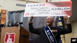 Cheng "Charlie" Saephan holds display check above his head after speaking during a news conference where it was revealed that he was one of the winners of the $1.3 billion Powerball jackpot at the Oregon Lottery headquarters on April 29, 2024, in Salem, Ore.