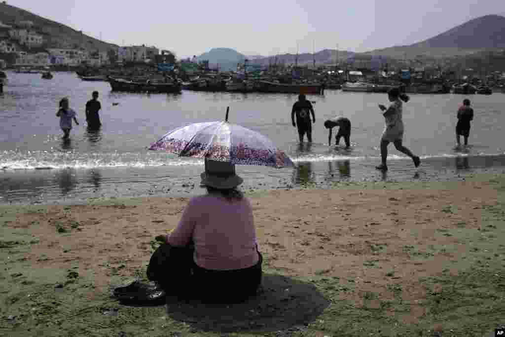 Una mujer descansa con un paraguas frente a los botes de pescadores el día de San Pedro, santo patrón católico de los pescadores, en Pucusana, Perú, el jueves 29 de junio de 2023.