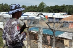 FILE - A Myanmar guard patrols outside a fenced-in camp during a government-organized media tour to a no-man's land between Myanmar and Bangladesh, near Taungpyolatyar village, Maung Daw, northern Rakhine State, Myanmar, June 29, 2018.