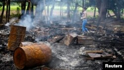 Seorang wartawan tengah berjalan di antara puing-puing rumah yang hangus terbakar di desa Shwe Lay, di pinggir wilayah Thandwe, negara bagian Rakhine, Burma (2/10).