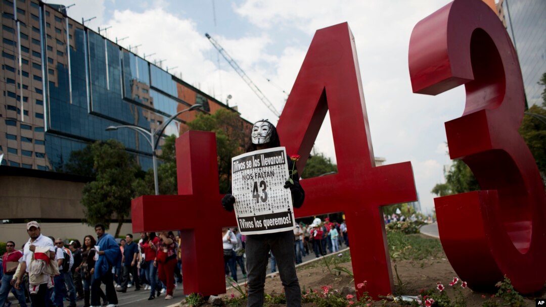 FILE - A masked protester poses with a sign reading "We are missing 43.