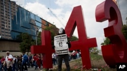 FILE - A masked protester poses with a sign reading "We are missing 43.