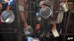 Palestinians gather to receive food being distributed along the roadside at the Nuseirat refugee camp in the central Gaza Strip on Jan. 11, 2025, as U.S., Qatari and Egyptian mediators worked to reach a hostage deal and ceasefire.