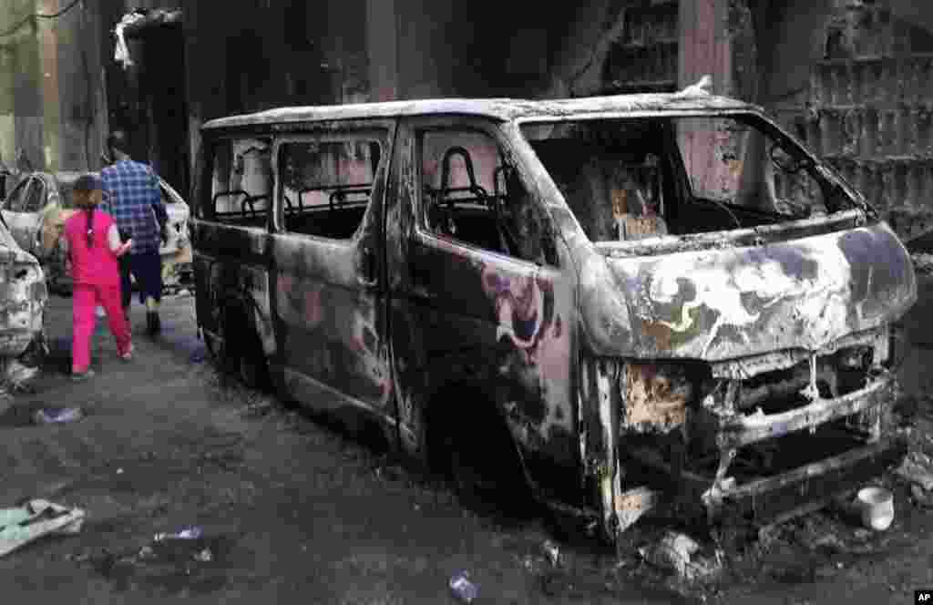 In this citizen journalism image provided by Shaam News Network, a Syrian man and girl walk past destroyed vehicles in Damascus, Syria, July 24, 2012.
