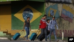 ARCHIVO - En esta fotografía del 9 de marzo de 2018, jóvenes venezolanos sacan su equipaje después de cruzar la frontera hacia Pacaraima, estado de Roraima, Brasil.