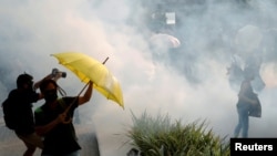 Anti-government demonstrators hold umbrellas against the tear gas during a protest in Hong Kong's tourism district of Tsim Sha Tsui, Oct. 27, 2019.