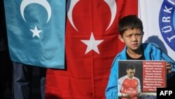 Seorang pendukung minoritas Muslim Uighur di China menunjukkan poster Mesut Ozil, pemain Arsenal asal Jerman yang berdarah Turki melintasi bendera Turkestan Timur dan Turki di Lapangan Beyazid, Istanbul, 14 Desember 2019. (Foto: AFP)