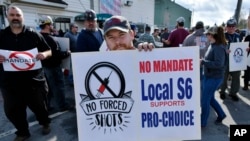 Alec Young, un armador de barcos en Bath Iron Works, en el centro, se manifiesta en contra de los mandatos de la vacuna COVID-19 fuera del astillero, el 22 de octubre de 2021, en Bath, Maine.