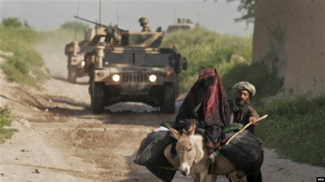 Konvoi pasukan NATO saat melakukan patroli di wilayah pedalaman, sementara seorang wanita Afghanistan menaiki keledai dengan didampingi suaminya.