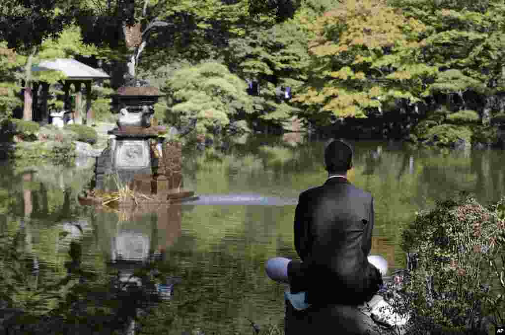 Seorang pria duduk di atas batu dan melakukan meditasi di taman Hibiya di Tokyo, Jepang. 