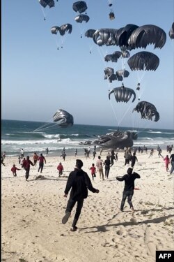 Orang-orang Palestina berlarian mendekati parasut yang membawa parsel-parsel bantuan makanan yang dikirim oleh Amerika Serikat lewat udara, di Pantai Jalur Gaza, Sabtu, 2 Maret 2024. (Foto: AFP)