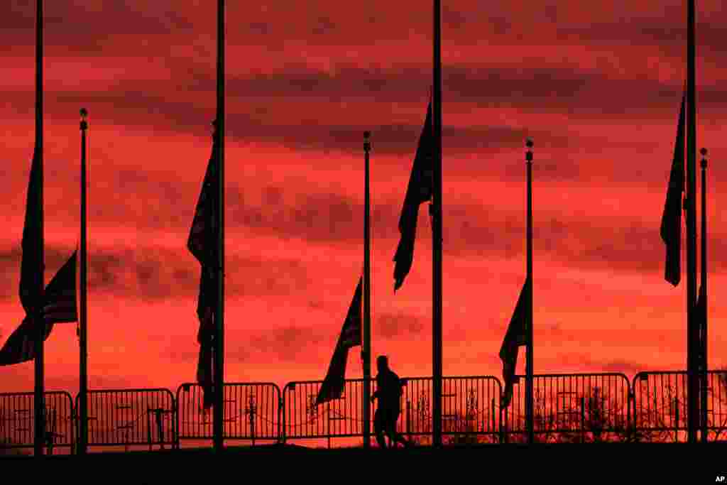 A runner passes under the flags hanging at half-staff surrounding the Washington Monument at day break in Washington, D.C.