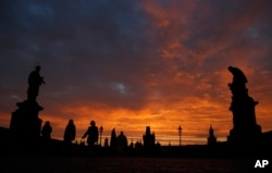 FILE - People cross the medieval Charles Bridge as the sun rises in Prague, Czech Republic, Thursday, Oct. 17, 2013. (AP Photo/Petr David Josek)