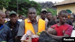 Abajejwe gutabara bafise umwana yarokotse igihe umwavu wasenyukira ku mazu mu micungararo ya Conakry, Gineya. 