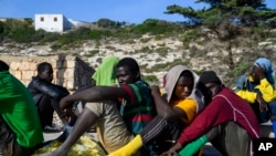 FILE - Migrants sit in Lampedusa Island, Italy, Friday, Sept. 15, 2023.