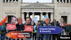 Cidadãos seguram cartazes durante um protesto à margem da Conferência de Segurança de Munique (MSC), em Munique, Alemanha, a 14 de fevereiro de 2025