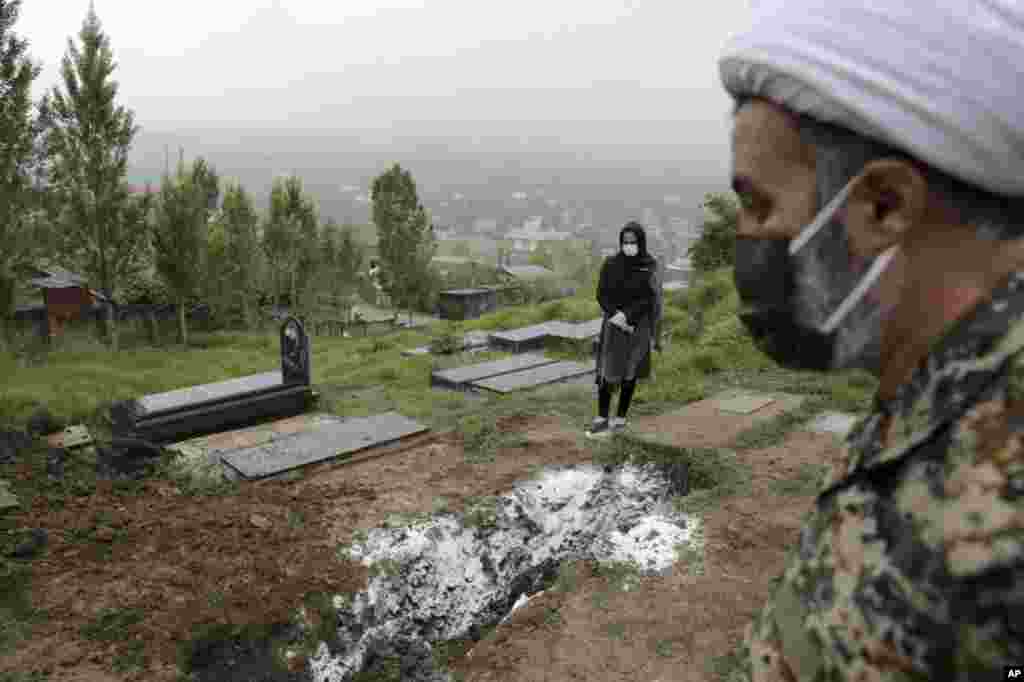 A woman wearing a mask and gloves prays at the grave of her mother, who died from the new coronavirus, at a cemetery in the outskirts of the city of Babol, Iran, April 30, 2020. 