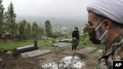 FILE - A woman wearing a mask and gloves prays at the grave of her mother, who died from the new coronavirus, at a cemetery in the outskirts of the city of Babol, Iran, April 30, 2020.