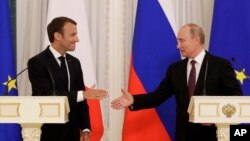 Russian President Vladimir Putin (R) and French President Emmanuel Macron, shake hands after their joint news conference following the talks at the Konstantin palace with the statue of the Peter The Great in the background just outside St. Petersburg, Russia, May 24, 2018.