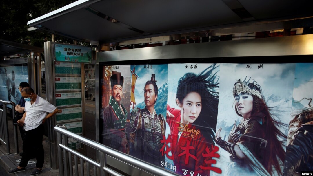 Orang-orang berdiri di dekat iklan yang mempromosikan film Disney "Mulan" di halte bus di Beijing, Cina, 9 September 2020. (Foto: REUTERS / Carlos Garcia Rawlins)