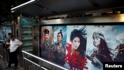 Orang-orang berdiri di dekat iklan yang mempromosikan film Disney "Mulan" di halte bus di Beijing, Cina, 9 September 2020. (Foto: REUTERS / Carlos Garcia Rawlins)