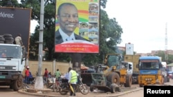 People pass in front of an electoral campaign poster for incumbent President Alpha Conde in Conakry, Guinea, Sept. 10, 2015. 