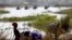 FILE - Nigerians fleeing Boko Haram attacks continue to enter Chad; men on camels cross the water as a woman washes clothes in Lake Chad at Ngouboua, Jan. 19, 2015.