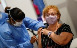 A health care worker administers a dose of the Oxford-AstraZeneca coronavirus vaccine, marketed by the Serum Institute of India (SII) as COVISHIELD, to a woman at a vaccination center in Buenos Aires, Argentina, Feb. 22, 2021.