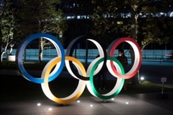 Two men chat behind the Olympic rings near the New National Stadium in Tokyo, March 24, 2020.