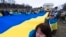 Los ucranianos y sus partidarios llevan una enorme bandera ucraniana durante una manifestación en el National Mall cerca del Monumento a Lincoln en Washington, conmemorando dos años desde la guerra. [Foto: Archivo/AP/Manuel Balce Ceneta]. 
