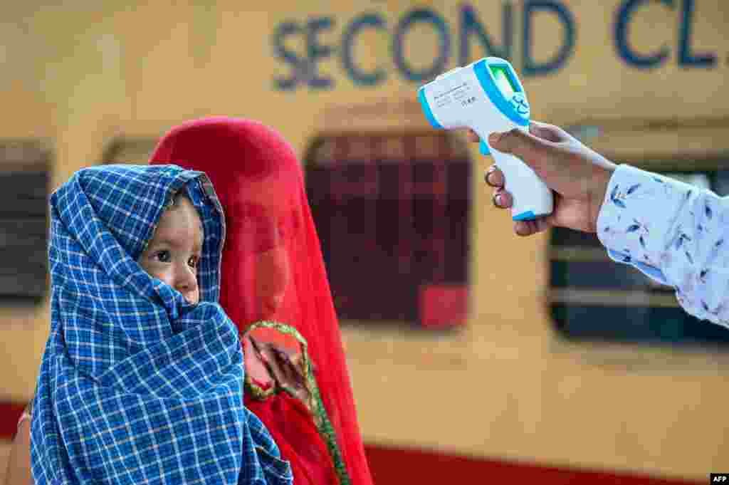 A health worker checks the body temperature of a passenger during a COVID-19 screening as she arrives with her child at a railway platform, in Mumbai, India.
