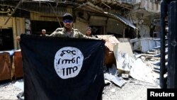 FILE - A member of the Emergency Response Division holds an Islamic State militants flag in the Old City of Mosul, Iraq, July 10, 2017. 