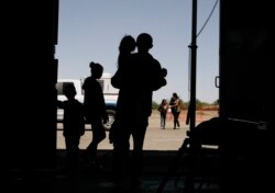 FILE - Migrants, mainly from Central America, guide their children through the entrance of a World War II-era bomber hanger in Deming, N.M., May 22, 2019.