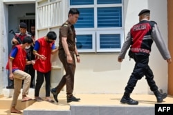 Dua pemuda (kiri dan kedua dari kiri) dikawal petugas saat akan menghadiri sidang di pengadilan Syariah di Banda Aceh, 24 Februari 2025. Keduanya dijatuhi hukuman cambuk karena melakukan hubungan seks sesama jenis. (CHAIDEER MAHYUDDIN / AFP)