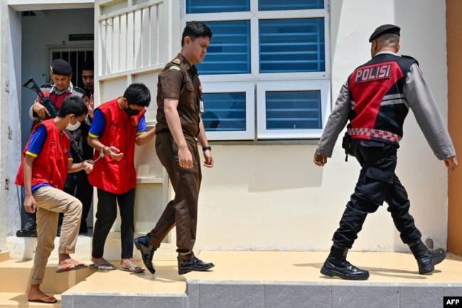Dua pemuda (kiri dan kedua dari kiri) dikawal petugas saat akan menghadiri sidang di pengadilan Syariah di Banda Aceh, 24 Februari 2025. Keduanya dijatuhi hukuman cambuk karena melakukan hubungan seks sesama jenis. (CHAIDEER MAHYUDDIN / AFP)