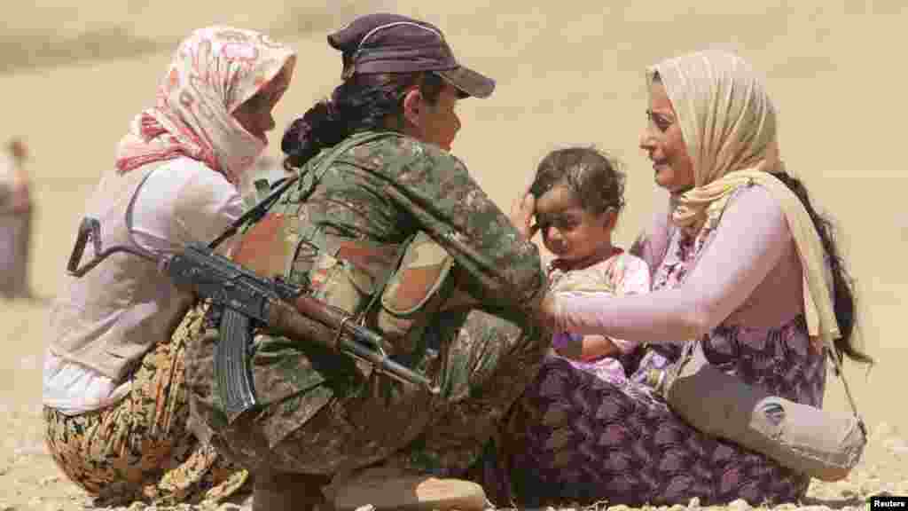 Displaced people from the minority Yazidi sect, fleeing violence from forces loyal to the Islamic State in Sinjar town, get help from a member of the Kurdish People's Protection Units (YPG) near the Syrian border town of Elierbeh of Al-Hasakah Governorate