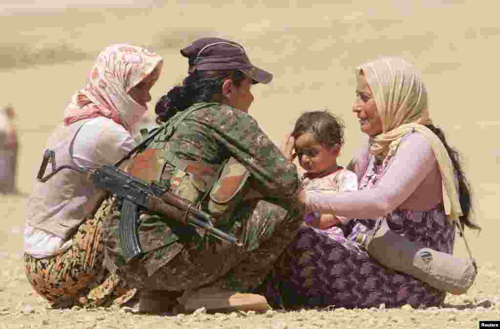 Displaced people from the minority Yazidi sect, fleeing violence from forces loyal to the Islamic State in Sinjar town, get help from a member of the Kurdish People's Protection Units (YPG) near the Syrian border town of Elierbeh of Al-Hasakah Governorate
