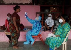 A health worker in personal protective equipment (PPE) checks the temperature of a resident with an electronic thermometer during a check up campaign for the coronavirus disease (COVID-19), in Mumbai, India, July 13, 2020.