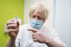 FILE - Britain's Prime Minister Boris Johnson holds a vial of Astra Zeneca coronavirus vaccine during a visit to a coronavirus vaccination center in Orpington, England, Feb. 15, 2021.