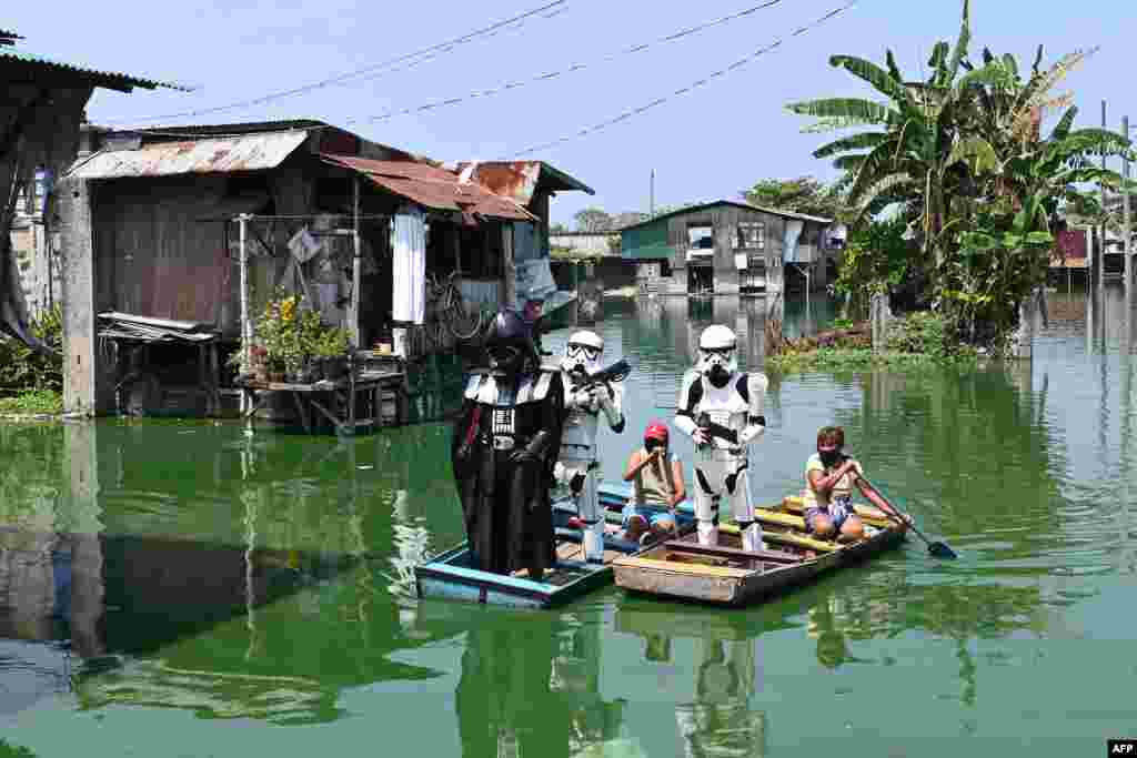 Local youth representatives dressed as Stormtroopers and Darth Vader (L-in black) from the Star Wars film patrol in a wooden boat around a submerged village to remind residents to stay at home during the enhanced community quarantine in suburban Manila, Philippines.