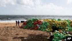 Sri Lankans walk past a pile of plastic pellets washed ashore from the fire damaged container ship MV X-Press Pearl at Kapungoda, on the outskirts of Colombo, Sri Lanka, June 11, 2021.