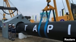 Workers stand near a gas pipe during the launching ceremony of construction work of the TAPI project on the Afghan section of a natural gas pipeline that will link Turkmenistan through Afghanistan to Pakistan and India, near the town of Serhetabat,Turkmenistan, Feb. 23, 2018.