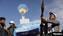 FILE - A Houthi follower holds a rocket launcher as others carry a cutout banner portraying a cargo ship seized by Houthis, during a parade in Sanaa, Yemen, on Feb. 7, 2024. The U.S. and U.K. on Feb. 27 sanctioned a Houthi militant after linking him to attacks in the Red Sea.