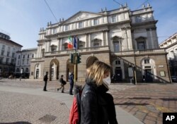 A woman wearing a protective mask walks past La Scala Opera house in Milan, Italy, Feb. 24, 2020.